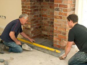 Two builders fitting a fireplace hearth using a spirit level
